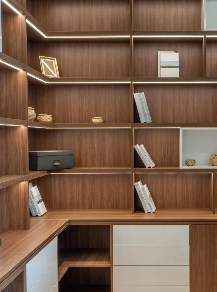 Built-in L-shaped desk with lit wood-finish shelving and white drawers